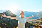Active senior woman standing with her arms outstretched looking happy and feeling free. Mature woman wearing headphones and listening to music while standing against a scenic mountain background