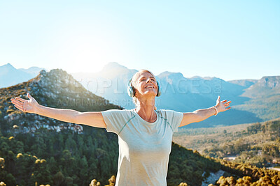 Buy stock photo Active senior woman standing with her arms outstretched looking happy and feeling free. Mature woman wearing headphones and listening to music while standing against a scenic mountain background