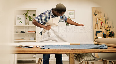 African american tailor looking at his material. Young fashion designer checking a roll of fabric. Creative entrepreneur looking at textiles in his studio. Small business owner working on designs