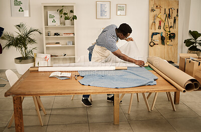 Buy stock photo African american designer looking at fabric. Young fashion designer checking roll of material. Seamstress checking his textiles. Creative entrepreneur working in his design studio.