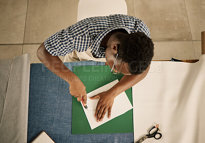 Fashion designer cutting fabric sample with knife from above. African American tailor cutting a piece of paper. Creative tailor cutting a sample from above. Seamstress cutting a sample at his table