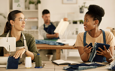 Buy stock photo Two fashion designers collaborating. Diverse businesswomen sewing together in a studio. Seamstress coworkers talking about denim material. Two creative entrepreneurs sewing together, talking.