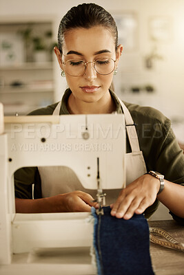 Mixed race designer sewing a piece of denim. Young tailor using a sewing machine. Creative businesswoman stitching a piece of fabric. Fashion designer sewing a piece of material