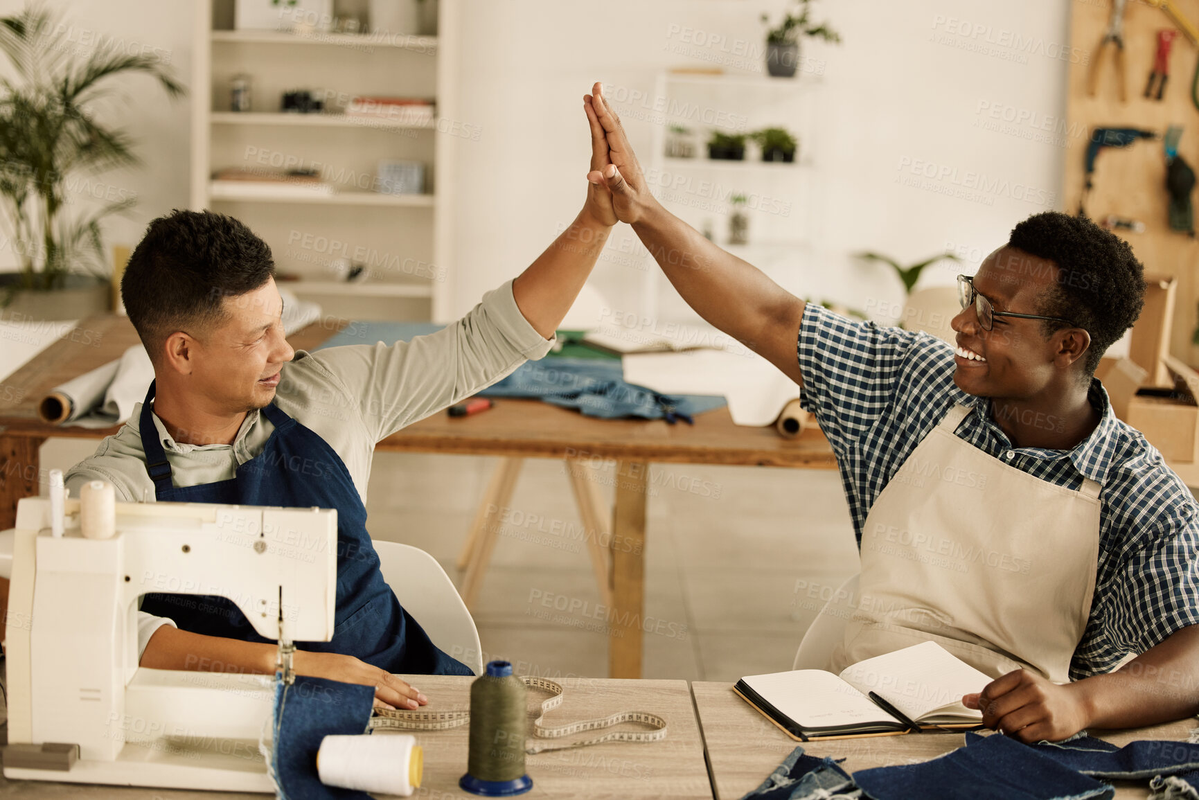 Buy stock photo Two designers giving each other a high five. Tailors celebrate together. Cheerful businesspeople collaborate together in their workshop. Diverse, excited designers celebrating.