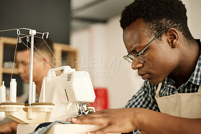 Buy stock photo Focused designer sewing fabric. Focused tailor using sewing machine. African American designer sewing a piece of denim. Young businessman working on a sewing machine. Tailor sewing a garment