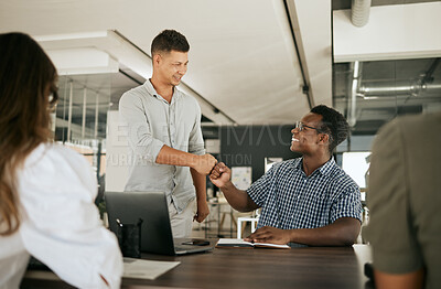 Two businessmen giving each other a fist bump at a desk. Mentor congratulating colleague on a job well done and being a fast learner in modern office. Friend working together in an office