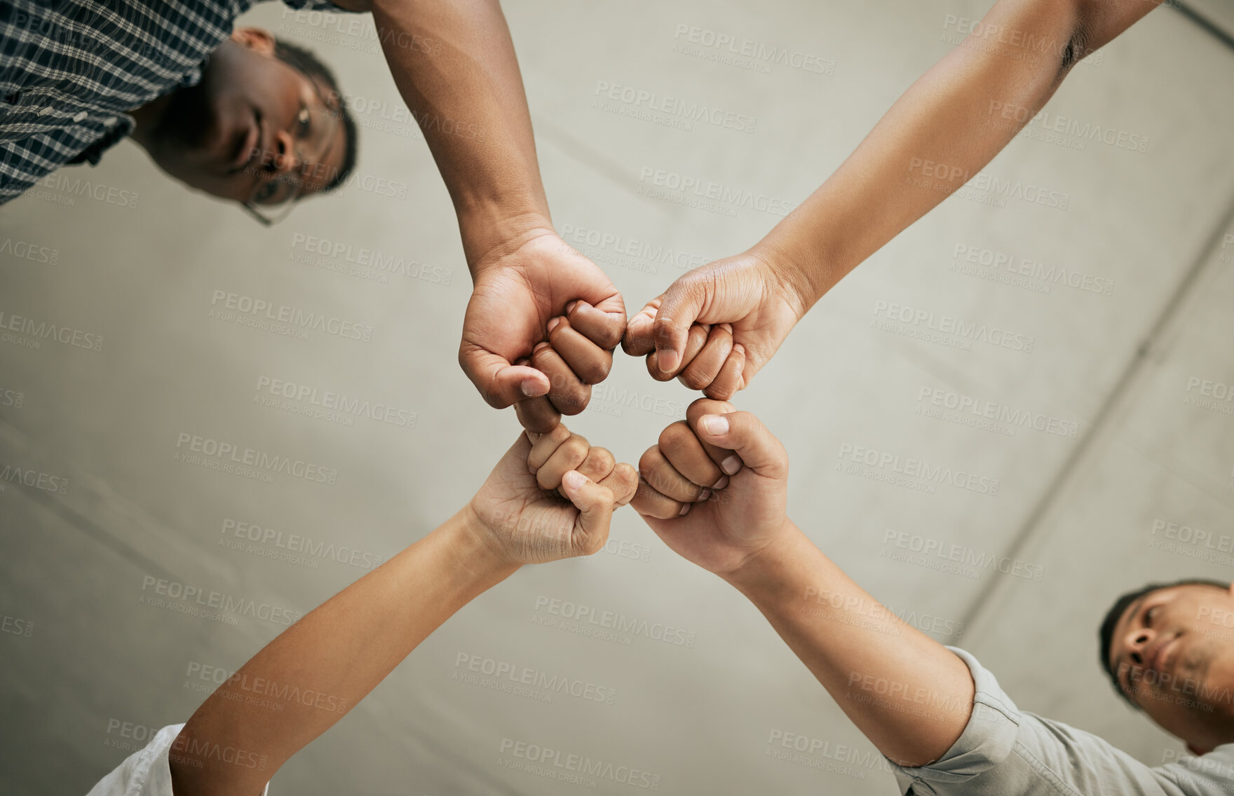 Buy stock photo Close up of creative businesspeople bringing their fists together from below. Diverse group of businesspeople standing together in a huddle showing strength in unity