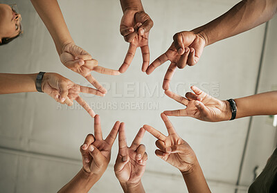 Close up of hands forming a star shape with the v-sign, from below. Group of diverse colleagues standing in a office showing unity and teamwork