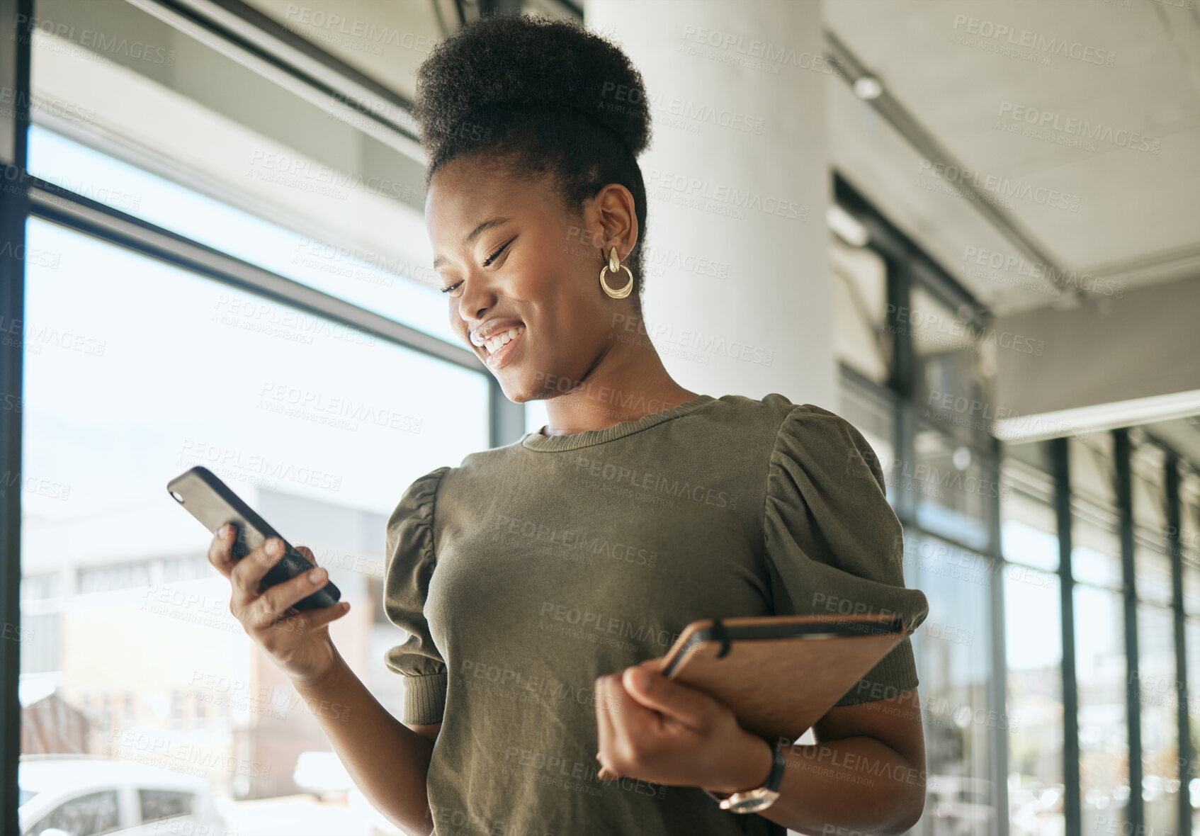 Buy stock photo African american business woman smiling while reading or texting on smartphone holding journal and walking in modern office. Smiling female entrepreneur using mobile app or browsing social media