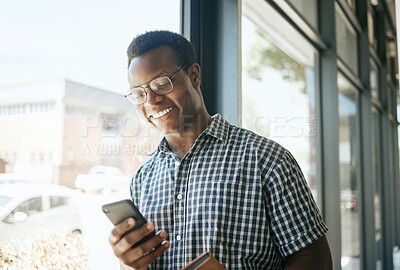 Happy african american business man entrepreneur leaning against a window in an office while reading or sending text on smartphone. Smiling entrepreneur chatting online or getting good news via app