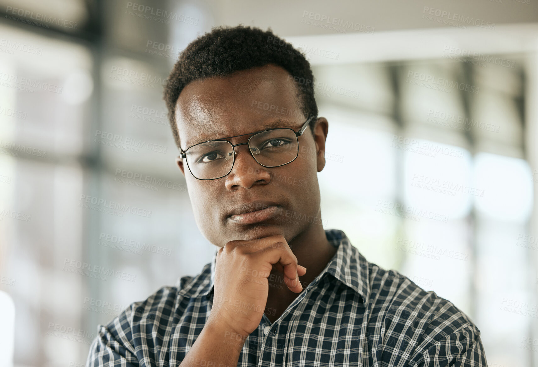 Buy stock photo Portrait of a serious young professional african american business man with glasses and hand on chin standing in an office and looking at camera