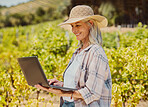 One smiling senior farmer holding and using a laptop on her vineyard. Happy elderly Caucasian woman browsing the internet around her crops and produce on wine farm in summer. Connected online on farm