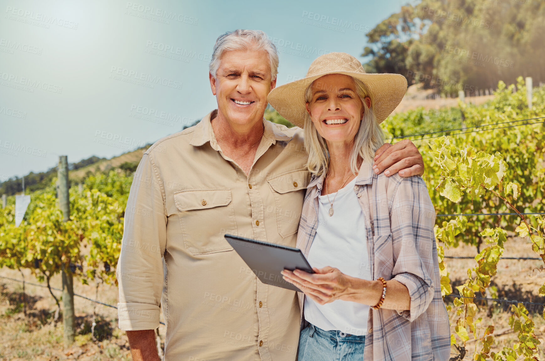 Buy stock photo Portrait of two happy senior farmers standing and using digital tablet on their vineyard. Smiling elderly man and woman bonding together on wine farm in summer. Happy couple embracing on wine farm