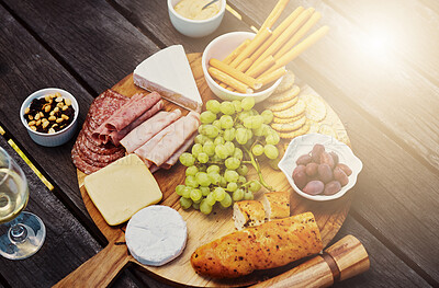 Above view of a variety of snacks on a tapas wooden board outside. Cheese, bread, fresh grapes and cold meats arranged for lunch on a vineyard. Food and wine tasting on a farm during a weekend