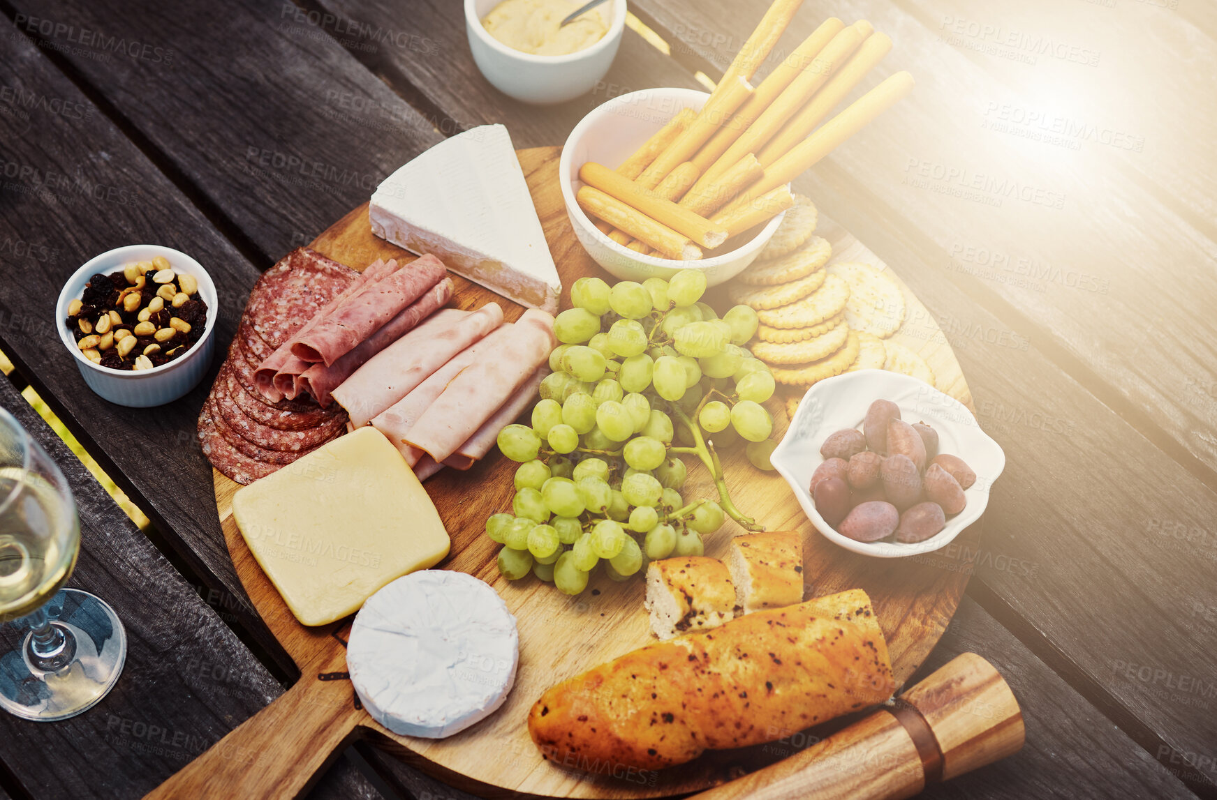 Buy stock photo Above view of a variety of snacks on a tapas wooden board outside. Cheese, bread, fresh grapes and cold meats arranged for lunch on a vineyard. Food and wine tasting on a farm during a weekend