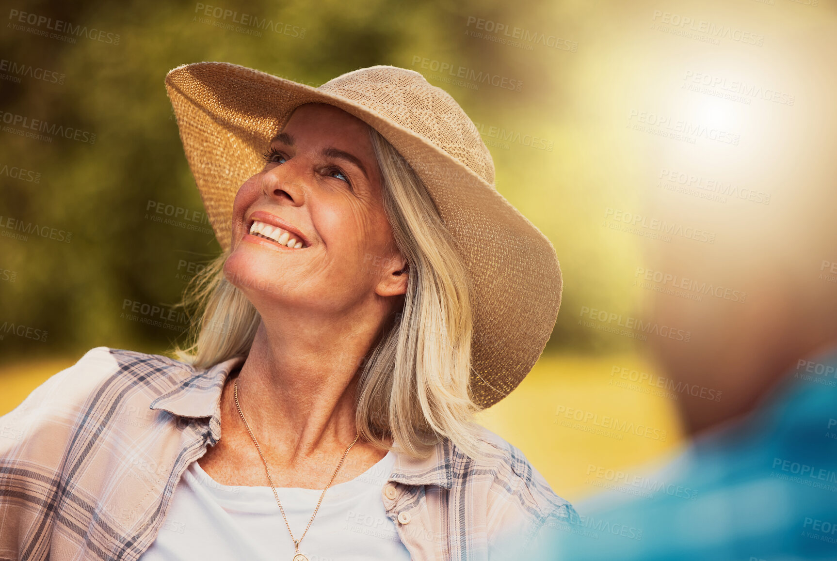 Buy stock photo Smiling senior woman enjoying a wine tasting day on a farm with friends. Happy caucasian woman wearing a hat while sitting and bonding on a vineyard. Elderly woman on a wine farm during the weekend
