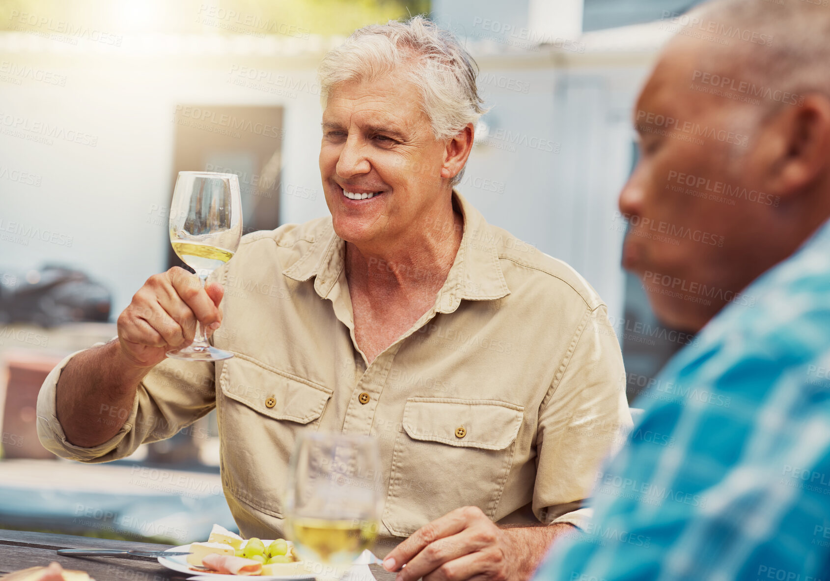 Buy stock photo Smiling senior man raising a wineglass on a vineyard with friends. Happy caucasian man sitting and bonding during a wine tasting on a farm over the weekend. Friends enjoying white wine and alcohol