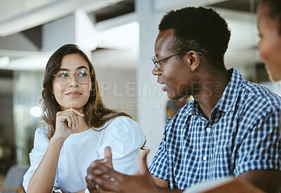 Buy stock photo Three young happy businesspeople having a meeting while sitting at a table at work. Business professionals talking and planning in an office together. African american man discussing a business strategy with coworkers
