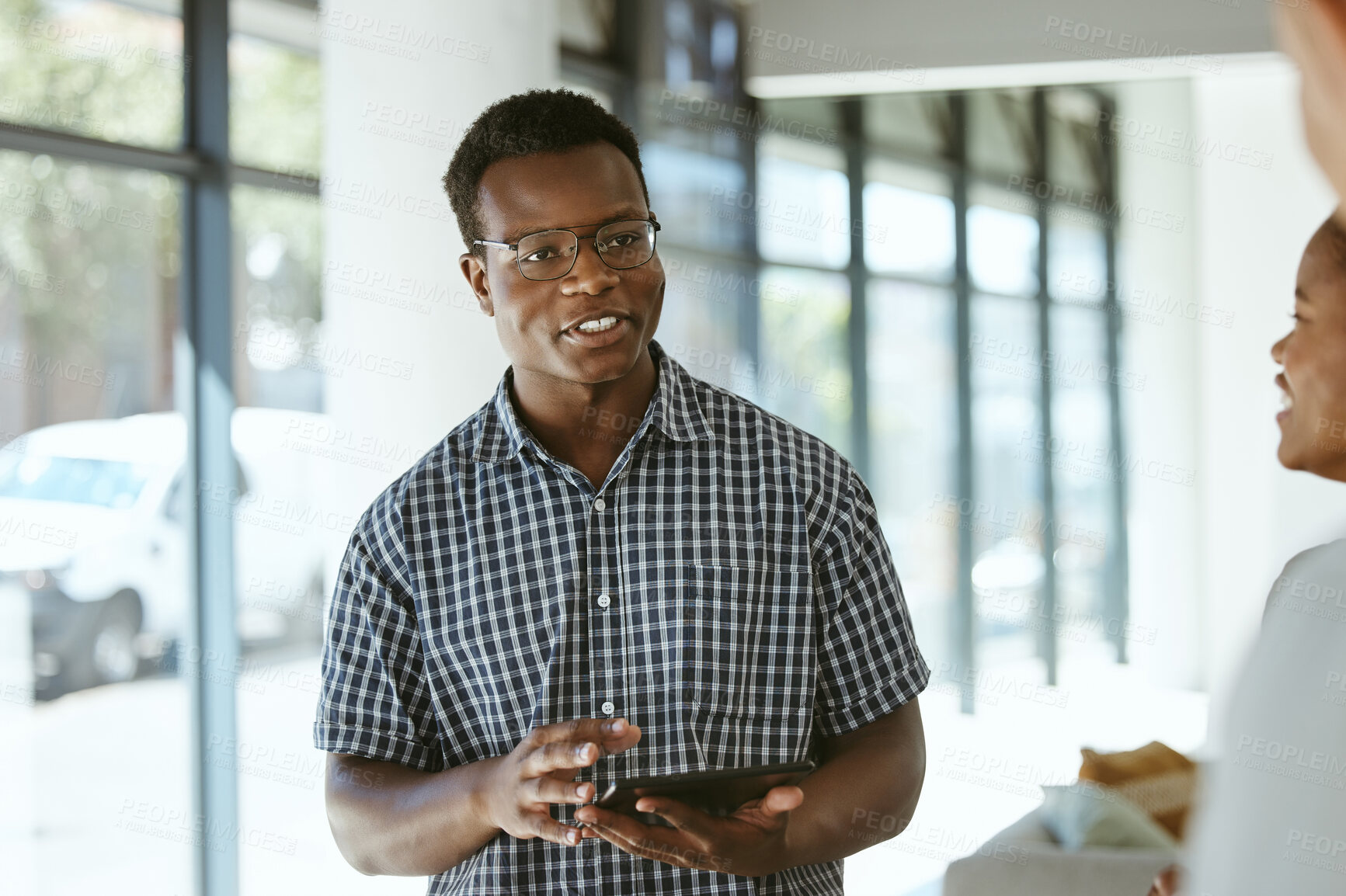 Buy stock photo Young happy african american businessman holding a digital tablet while talking with colleagues in an office at work. Male boss wearing glasses and talking to coworkers in a meeting at work