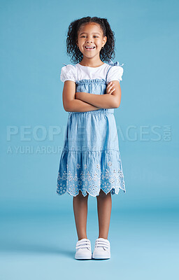 Buy stock photo Portrait of happy little girl standing with her arms crossed against blue studio background. Cheerful mixed race kid in casual denim dress and white tshirt