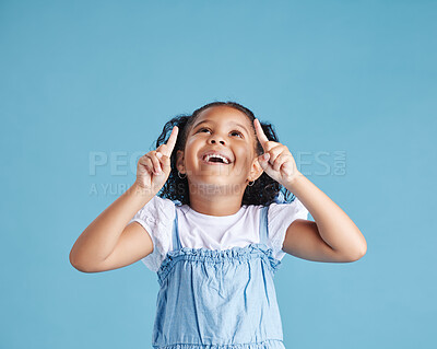 Excited little girl kid looking amazed and surprised while pointing her fingers up at copy space against blue studio background. Advertising childrens products