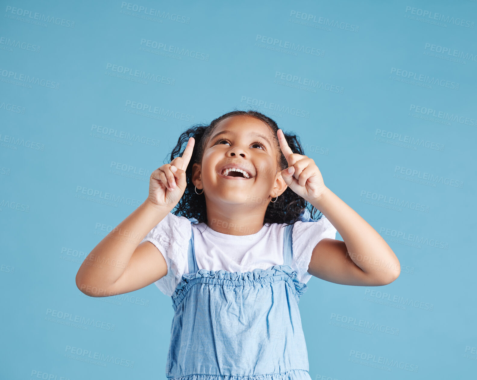 Buy stock photo Excited little girl kid looking amazed and surprised while pointing her fingers up at copy space against blue studio background. Advertising childrens products