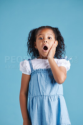 Buy stock photo Adorable hispanic little girl with hand on face and mouth open being surprised and shocked showing true astonished reaction against a blue studio background