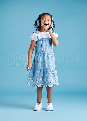 Buy stock photo Full length of an adorable little hispanic girl singing with her eyes closed while listening to music with wireless headphones enjoying her favourite song against a blue studio background