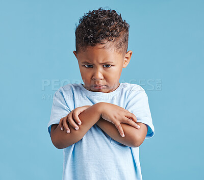 Offended little hispanic boy looking sad and upset while standing against a blue studio background. Unhappy preschooler standing with his arms crossed and looking down