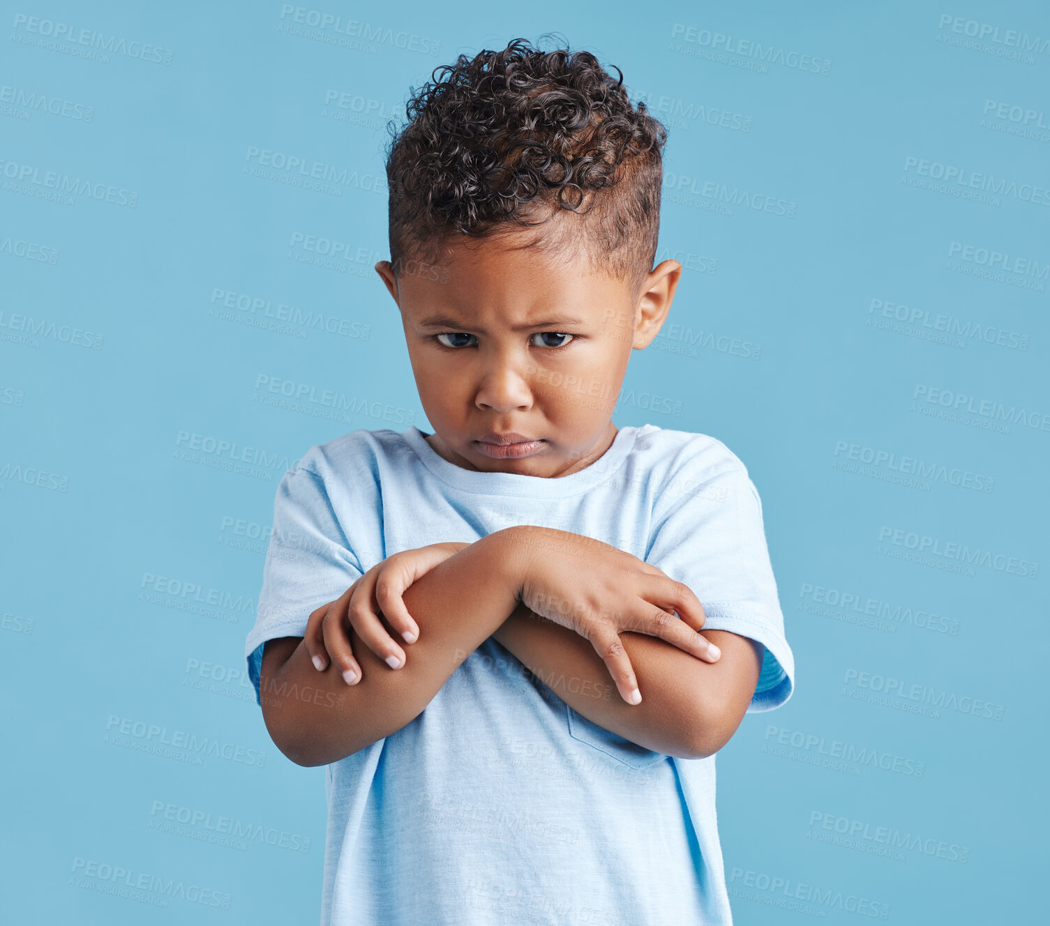 Buy stock photo Offended little hispanic boy looking sad and upset while standing against a blue studio background. Unhappy preschooler standing with his arms crossed and looking down