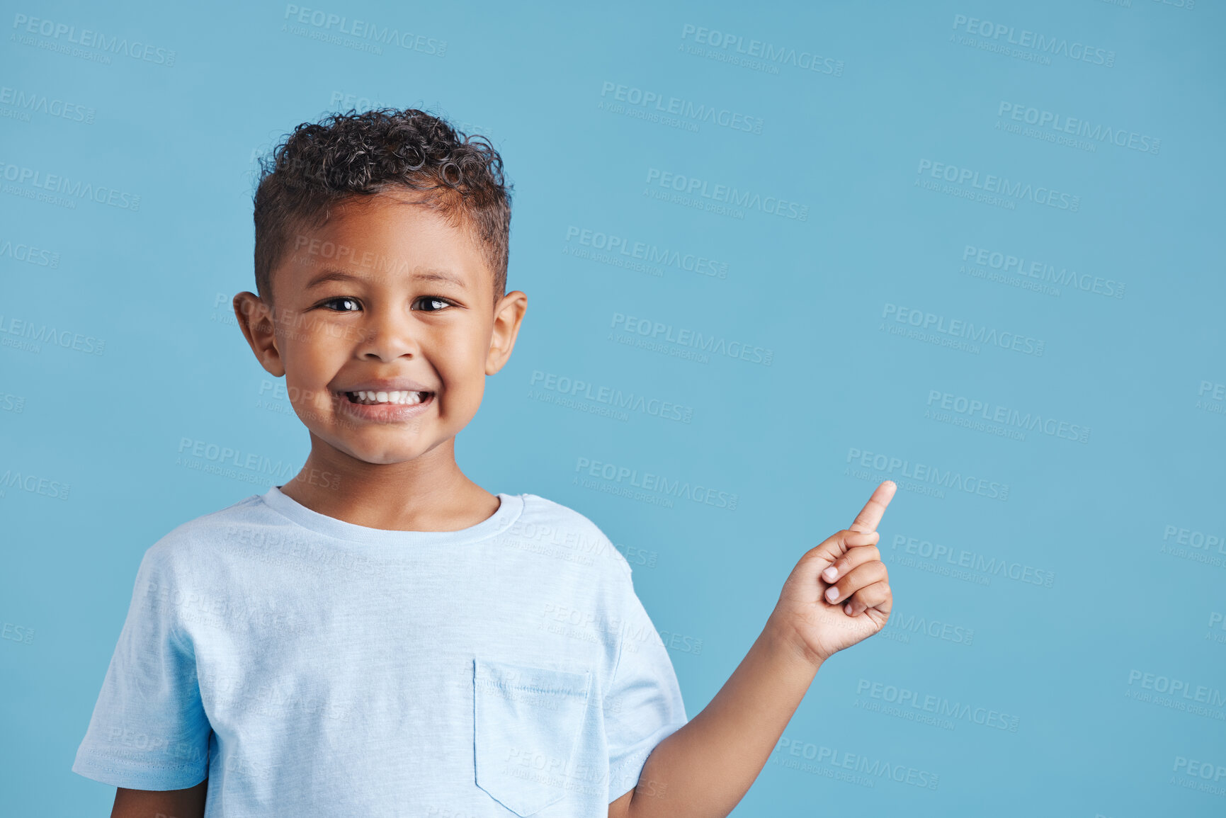 Buy stock photo Portrait of happy smiling little boy pointing his finger at copy space to the right against blue studio background. Cheerful hispanic kid with healthy dental smile in casual clothes