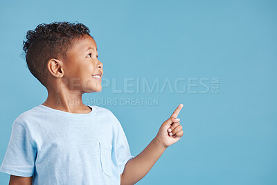 Close up of a happy smiling little boy looking up and pointing his finger at copy space to the right against blue studio background. Cheerful mixed race kid in casual clothes