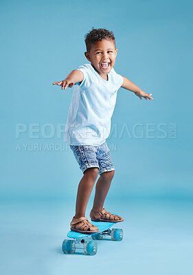 Buy stock photo Adorable little hispanic boy looking excited while balancing with his arms outstretched and riding his skateboard against a blue studio background