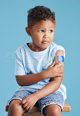 Vaccinated kid sitting on chair showing arm with adhesive bandage after vaccine injection standing against a blue studio background. Advertising vaccination against coronavirus. Child immunisation