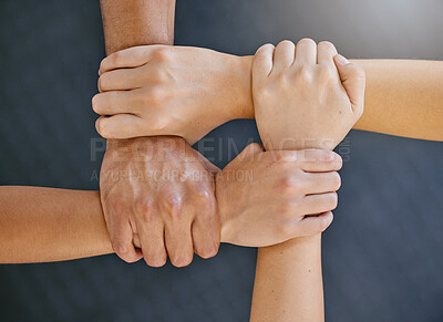 Closeup of diverse group of people from above holding each other\'s wrists in a circle to express unity, support and solidarity. Connected hands of multiracial community linked for teamwork in a huddle. Society join together for collaboration and equality
