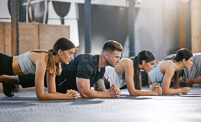 Diverse group of fit people doing bodyweight plank hold exercises together in a gym. Focused athletes training to build muscle, enhance upper body, strengthen core and increase endurance for workout in a fitness class