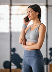 One active young hispanic woman talking on a cellphone while taking a break from exercise in a gym. Happy female athlete chatting on phone after her workout in a fitness centre