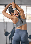 One active caucasian woman from behind stretching her arms and triceps by pulling elbow with hands towards spine behind head while exercising in a gym. Female athlete preparing body for training workout in a fitness centre
