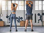 Two active caucasian athletes from behind behind stretching their arms and triceps by pulling elbow with hands towards spine behind head while exercising in a gym. Man and woman preparing body for training workout in a fitness centre