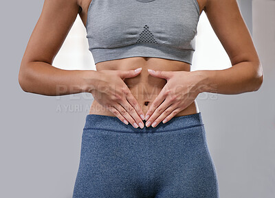Closeup of one fit caucasian woman framing hands around her slim belly to show weight loss while exercising against a grey background. Female athlete with toned body caring for gut digestion and wellbeing through active lifestyle and healthy diet