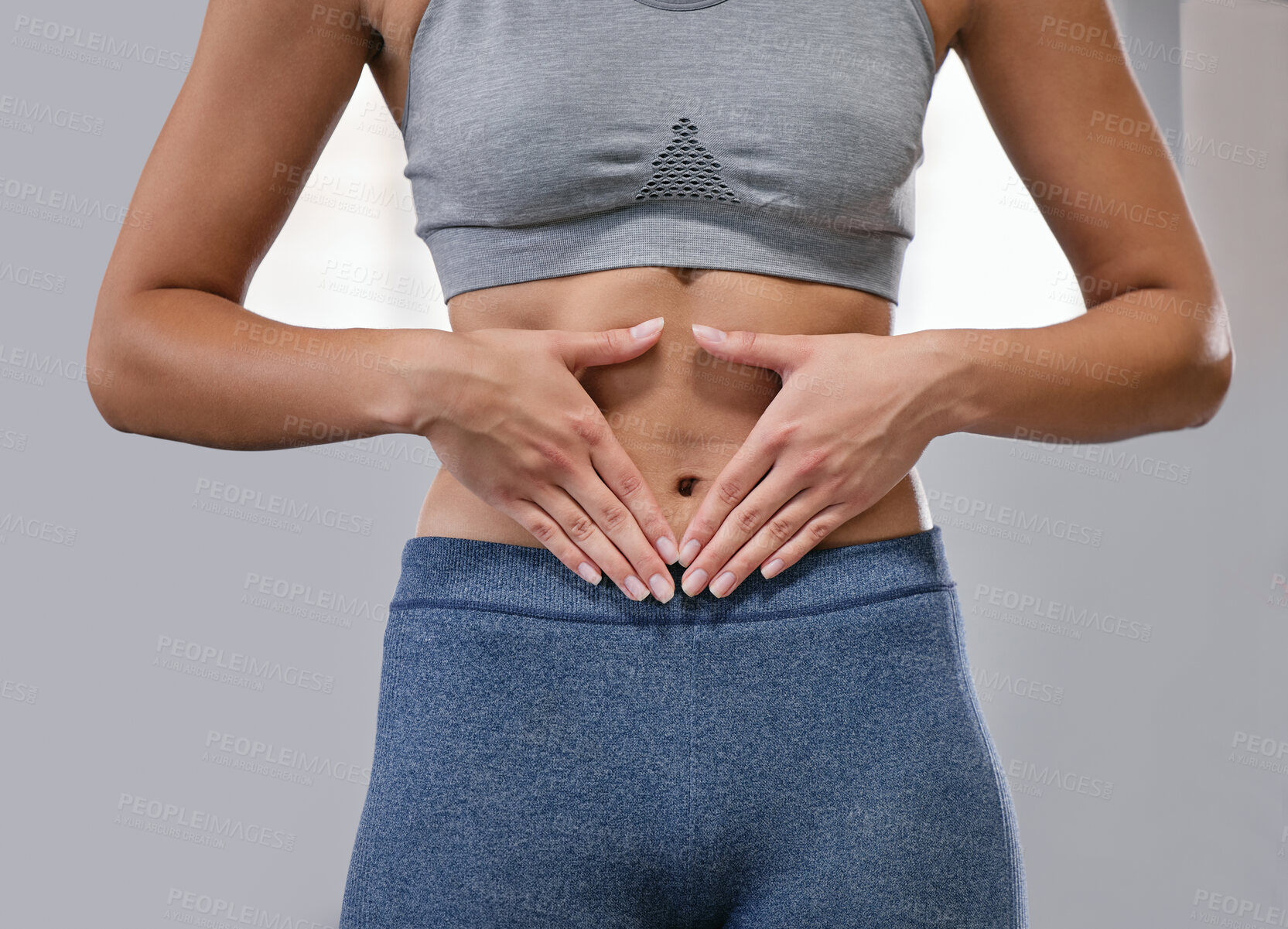 Buy stock photo Closeup of one fit caucasian woman framing hands around her slim belly to show weight loss while exercising against a grey background. Female athlete with toned body caring for gut digestion and wellbeing through active lifestyle and healthy diet