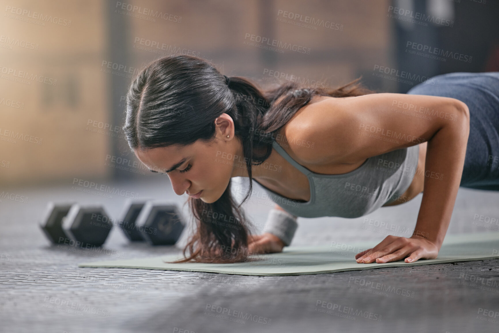 Buy stock photo One fit young hispanic woman doing bodyweight push up exercises while exercising in a gym. Focused female athlete doing press ups to build muscle, enhance upper body, strengthen core and increase endurance during a training workout
