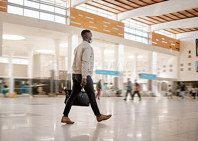 Buy stock photo Rear view of African american businessman travelling alone and walking in a train station while wearing a mask for protection against coronavirus
