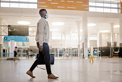 Buy stock photo African american businessman travelling alone and walking in a train station while wearing a mask for protection against coronavirus. Young black male on his way to work in a station in the morning