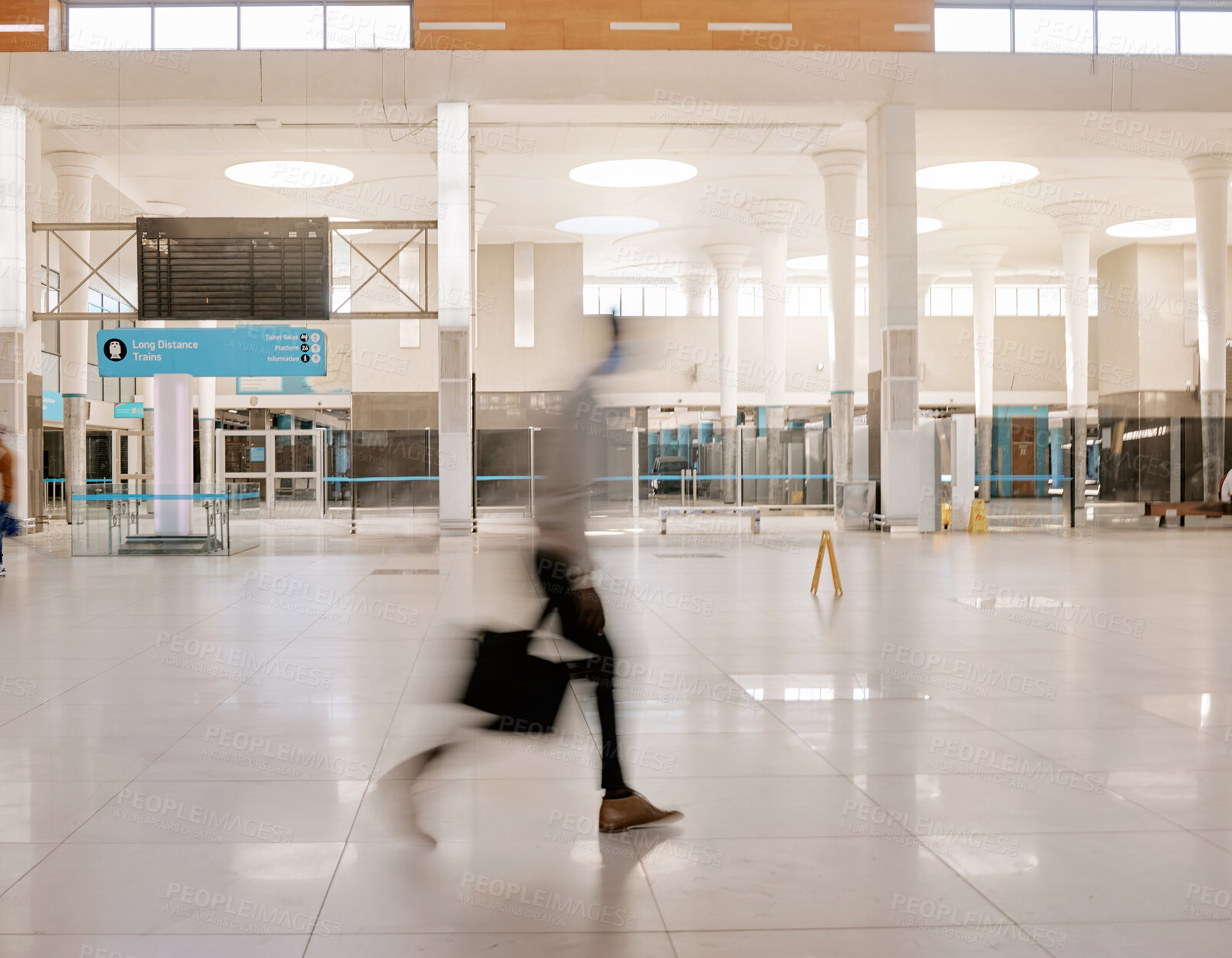 Buy stock photo Blurred businessman travelling alone and walking in a train station while wearing a mask for protection against coronavirus. Young black male on his way to work in a station in the morning