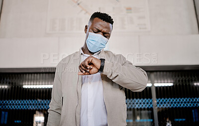 Buy stock photo African american businessman travelling alone and standing in a train station while checking his travel times on his watch while wearing a mask