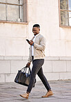 Black businessman travelling alone.A african american businessman walking around town with his luggage while looking at his smartphone and smiling in the city