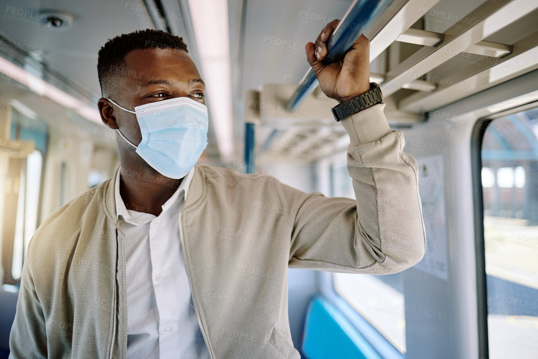 Buy stock photo Black businessman travelling alone and standing on a train on his way to work in the morning. African american male wearing a mask on his commute to the city