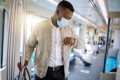 Buy stock photo Black businessman travelling alone. A young african american businessman standing on a train while checking the time on her watch and wearing a mask during his commute to the city