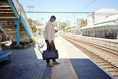 Buy stock photo Black Black businessman travelling alone. A young african american businessman waiting for a train at a railway station and using his wireless cellphone during his commute at a train station travelling alone
